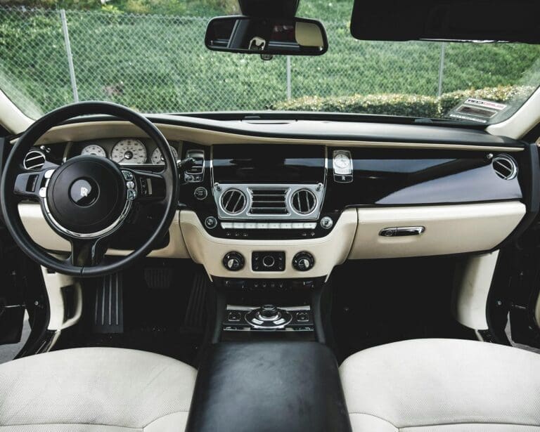 High angle interior of luxury car with leather seats and black wooden dashboard parked on street near green plants on sunny day